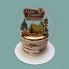 One-tier camping birthday cake with rustic brown and white buttercream, featuring a tent, campfire, trees, and 'Akila Caspian Happy 1st Birthday' topper.