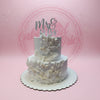 Two-tier white wedding cake with textured icing, white leaves, off-white berries, and a silver 
