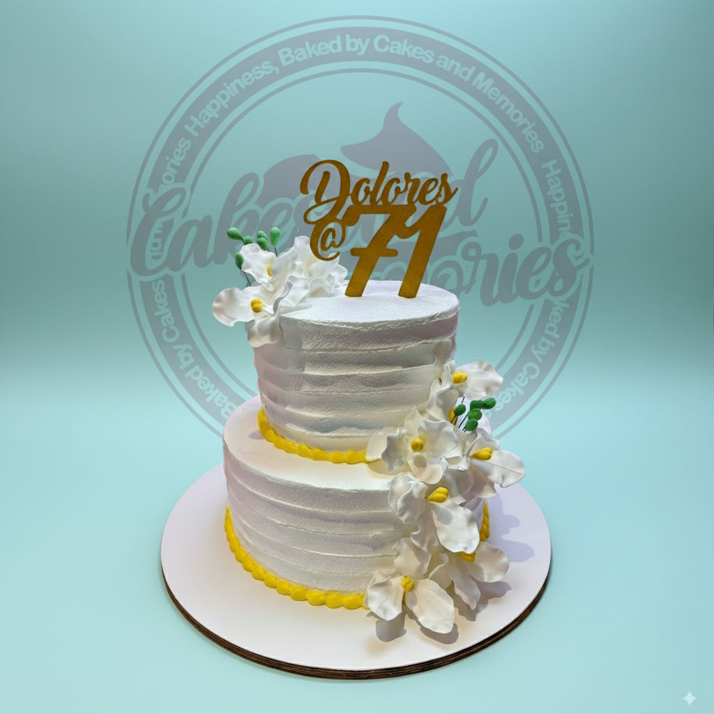 Two-tier white buttercream birthday cake with yellow trim, cascading white orchids, and a gold "Dolores @ 71" topper.
