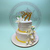 Two-tier white buttercream birthday cake with yellow trim, cascading white orchids, and a gold 