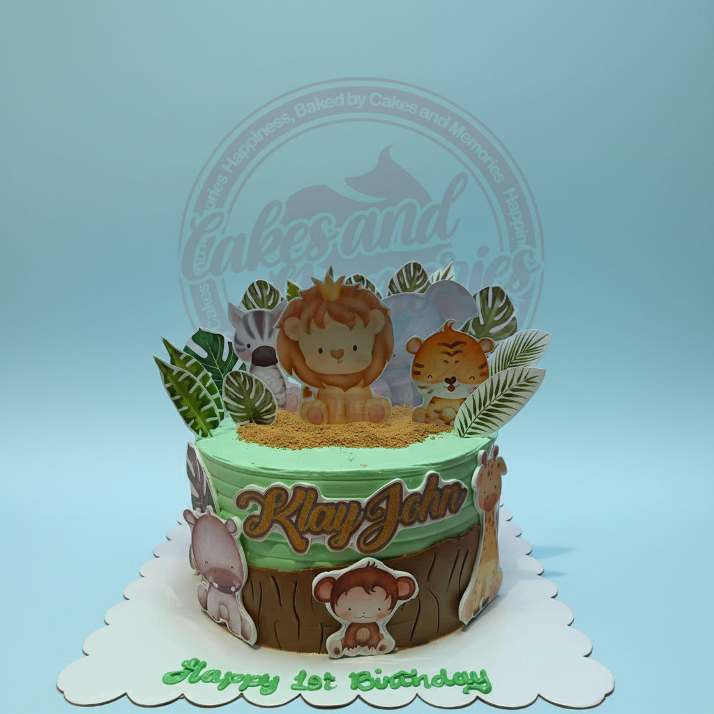 One-tier safari birthday cake for Klay John's 1st birthday, with cute animal and leaf toppers on green and brown buttercream.