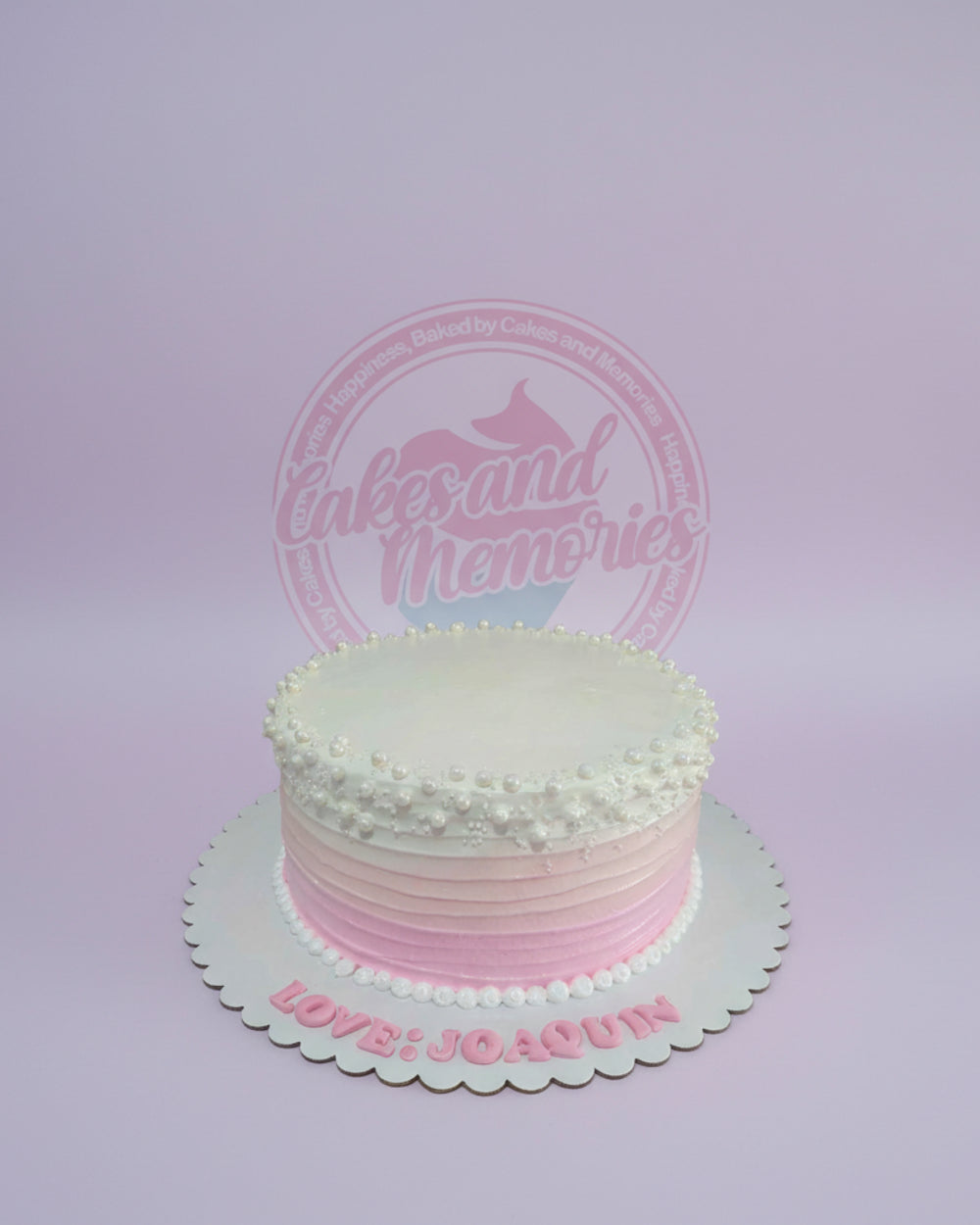 One-tier round buttercream cake with white to pink ombre icing, adorned with edible pearls and 'LOVE: JOAQUIN' text.
