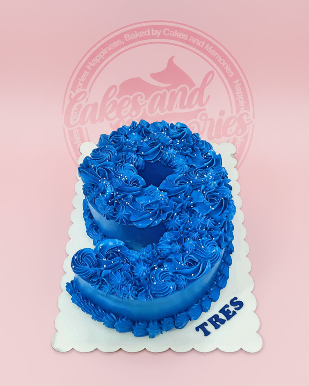Number 9 birthday cake with vibrant blue buttercream rosettes and white sprinkles, personalized with 'TRES' on the board.
