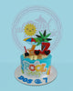 One-tier pool party birthday cake with bright blue icing, edible sand, sun, palm tree, beach chair, sunglasses, and 