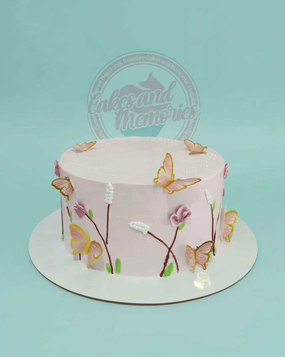 One-tier round pink buttercream cake with hand-piped botanical designs, white sprinkles, and gold-edged butterfly toppers.