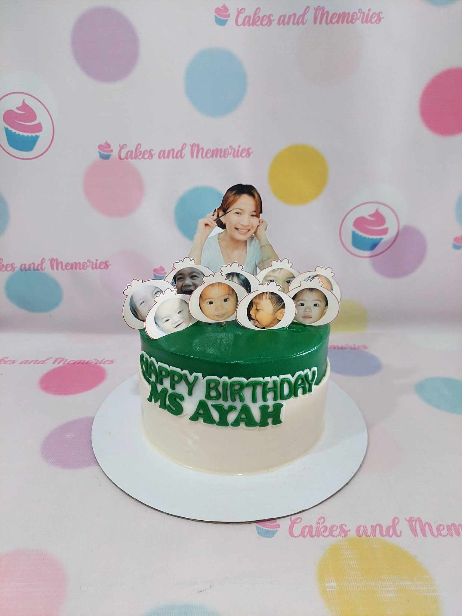 One-tier custom birthday cake with edible photo toppers of a smiling woman and babies, green and white icing, "HAPPY BIRTHDAY MS AYAH" in green letters.