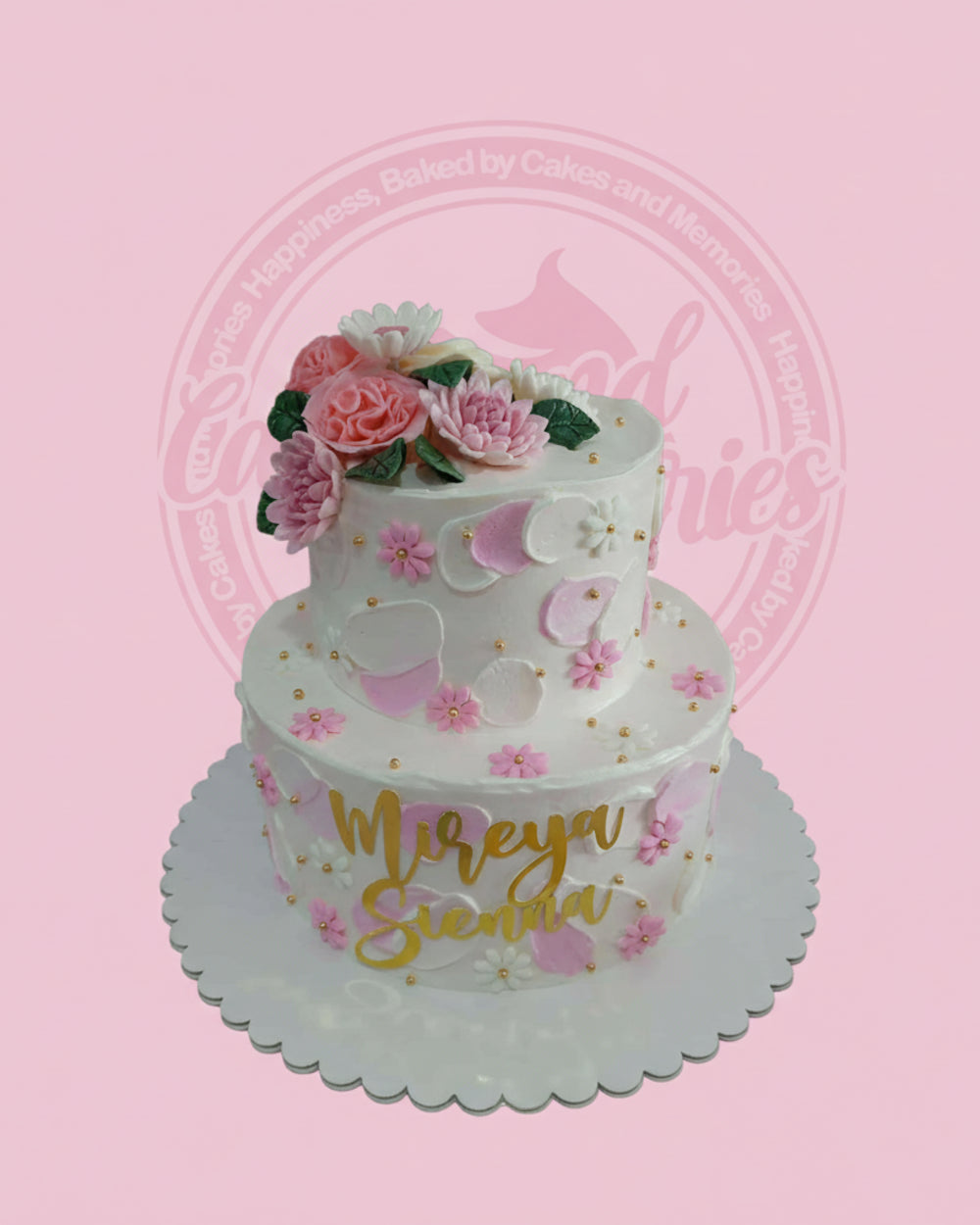 Two-tier white buttercream cake with pink and white hand-piped flowers, gold sprinkles, and a 'Mireya Sienna' name topper.