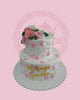 Two-tier white buttercream cake with pink and white hand-piped flowers, gold sprinkles, and a 'Mireya Sienna' name topper.