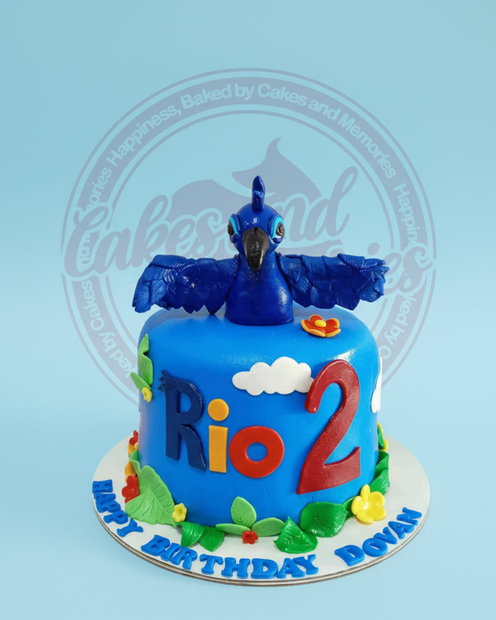 One-tier fondant Rio 2 birthday cake with sculpted Blu the macaw character, blue icing, 'Rio 2' text, and 'Happy Birthday Dovan'.