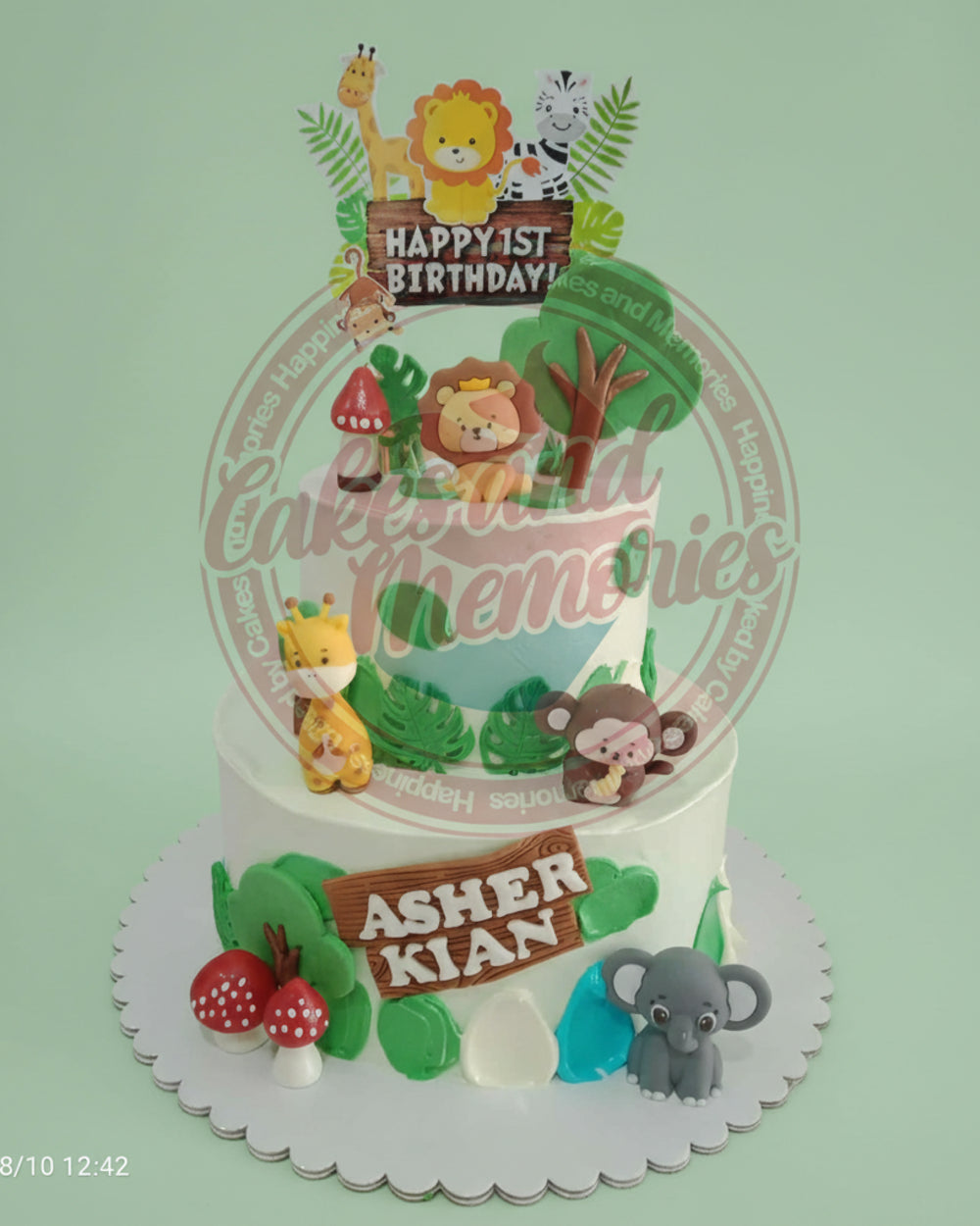 Two-tier safari 1st birthday cake for Asher Kian with cute lion, giraffe, zebra, monkey, elephant animals & jungle leaves.