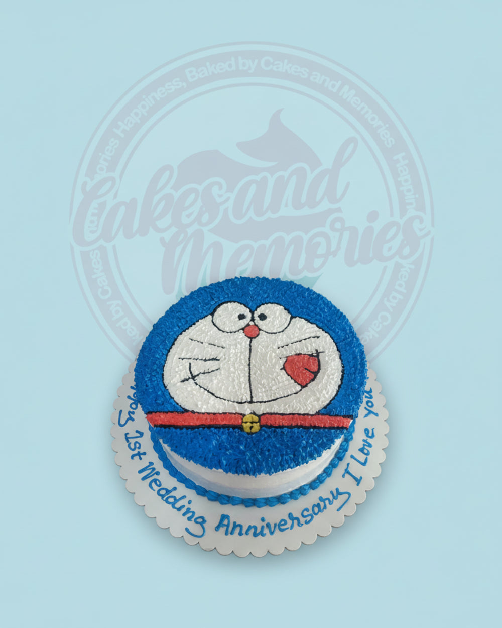 One-tier Doraemon cake featuring blue and white buttercream, hand-piped details, and '1st Wedding Anniversary' text on the board.