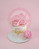One-tier round floral cake with pink and white watercolor icing, gold 'August' text, and pink peonies.