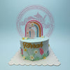 One-tier light blue custom birthday cake with a rainbow, number 5 topper, 'Farrah' in gold, and piped garden flowers.