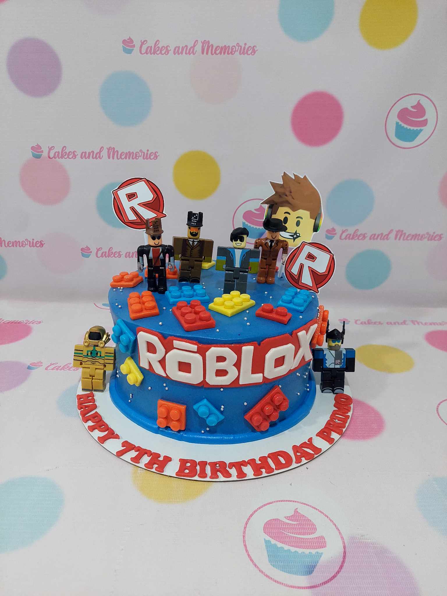 One-tier blue Roblox birthday cake with characters, building blocks, sprinkles, and 'Happy 7th Birthday Primo' lettering.