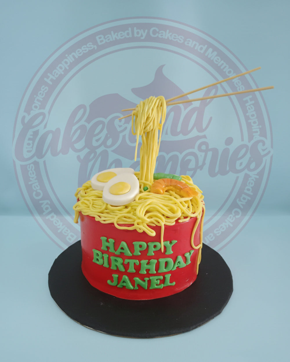 One-tier ramen birthday cake for Janel, featuring a red bowl, yellow noodles, fondant eggs, shrimp, veggies, and chopsticks.