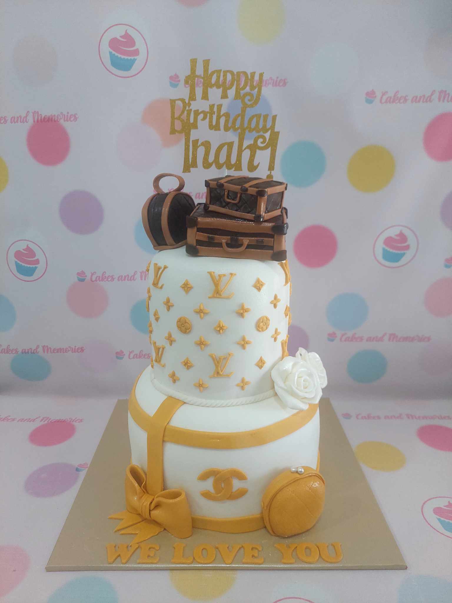 Two-tier luxury birthday cake with gold Louis Vuitton monograms, luggage, Chanel logo, and "Happy Birthday Inah!" topper.