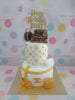 Two-tier luxury birthday cake with gold Louis Vuitton monograms, luggage, Chanel logo, and 