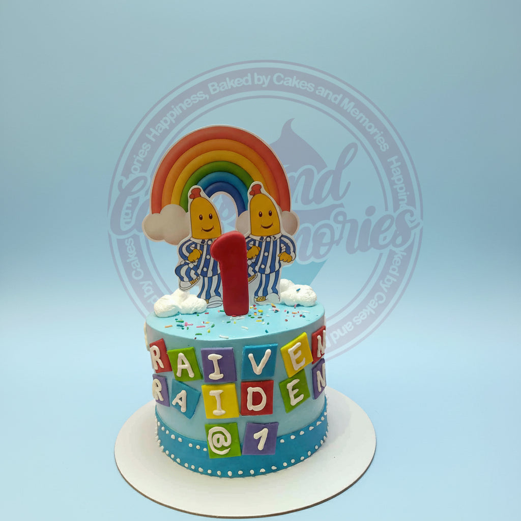 One-tier Bananas in Pyjamas birthday cake for twins Raiven and Raiden, with rainbow, '1' topper, and name blocks on blue icing.