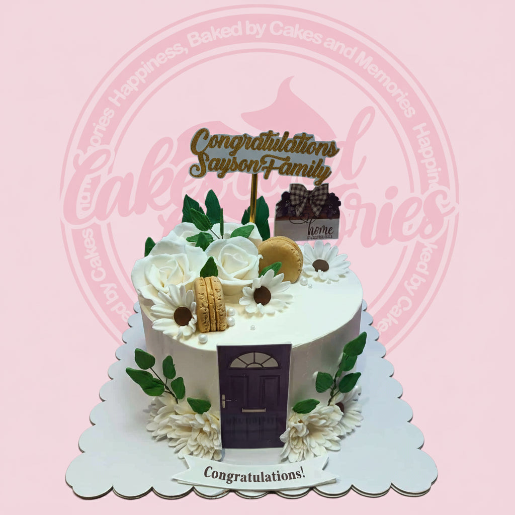 One-tier housewarming cake with white roses, daisies, green leaves, gold macarons, purple door, and 'Congratulations' topper.