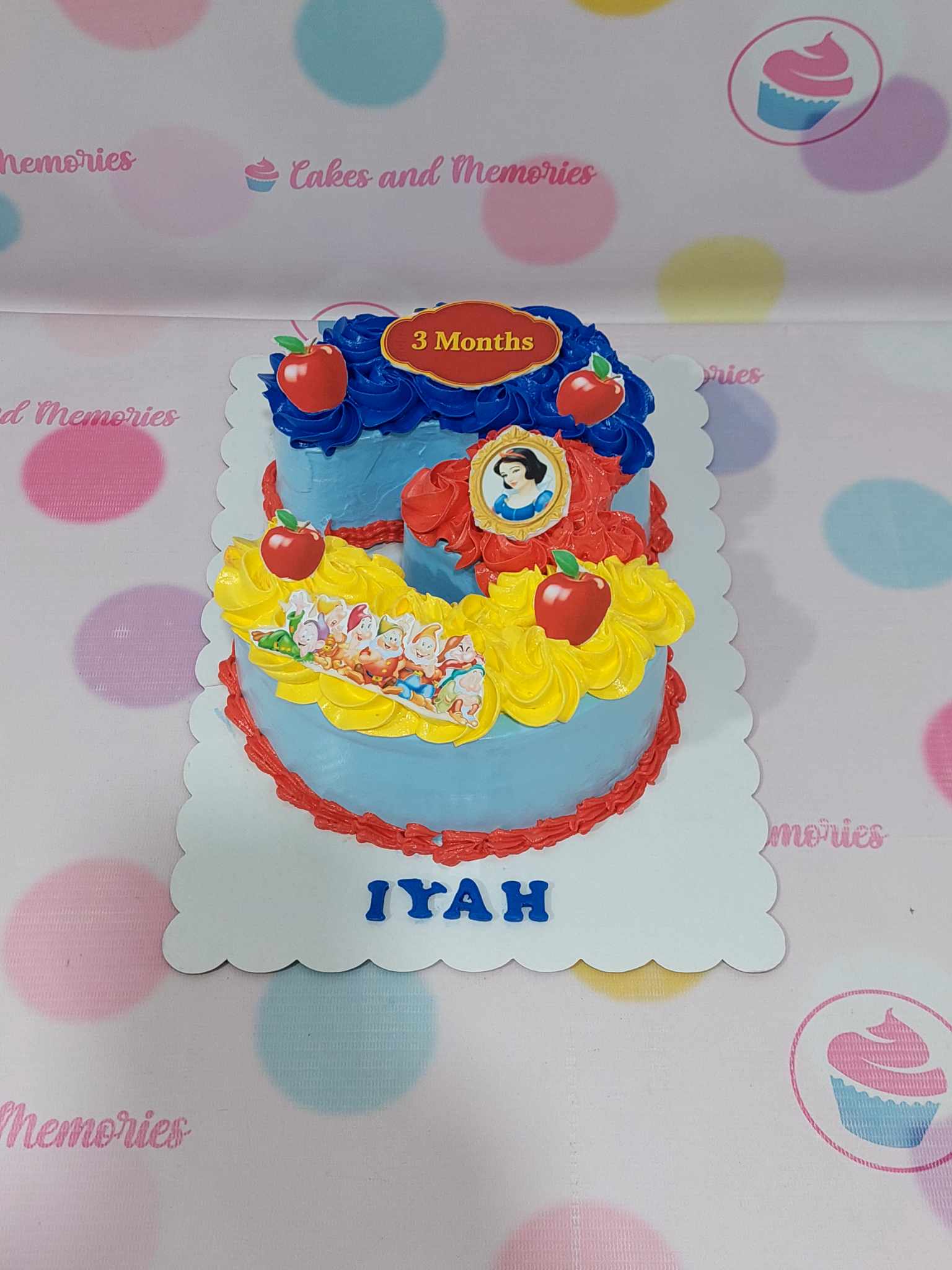 Number 3 custom buttercream cake with Snow White, Seven Dwarfs, red apples, and "IYAH 3 Months" text in blue, red, yellow.