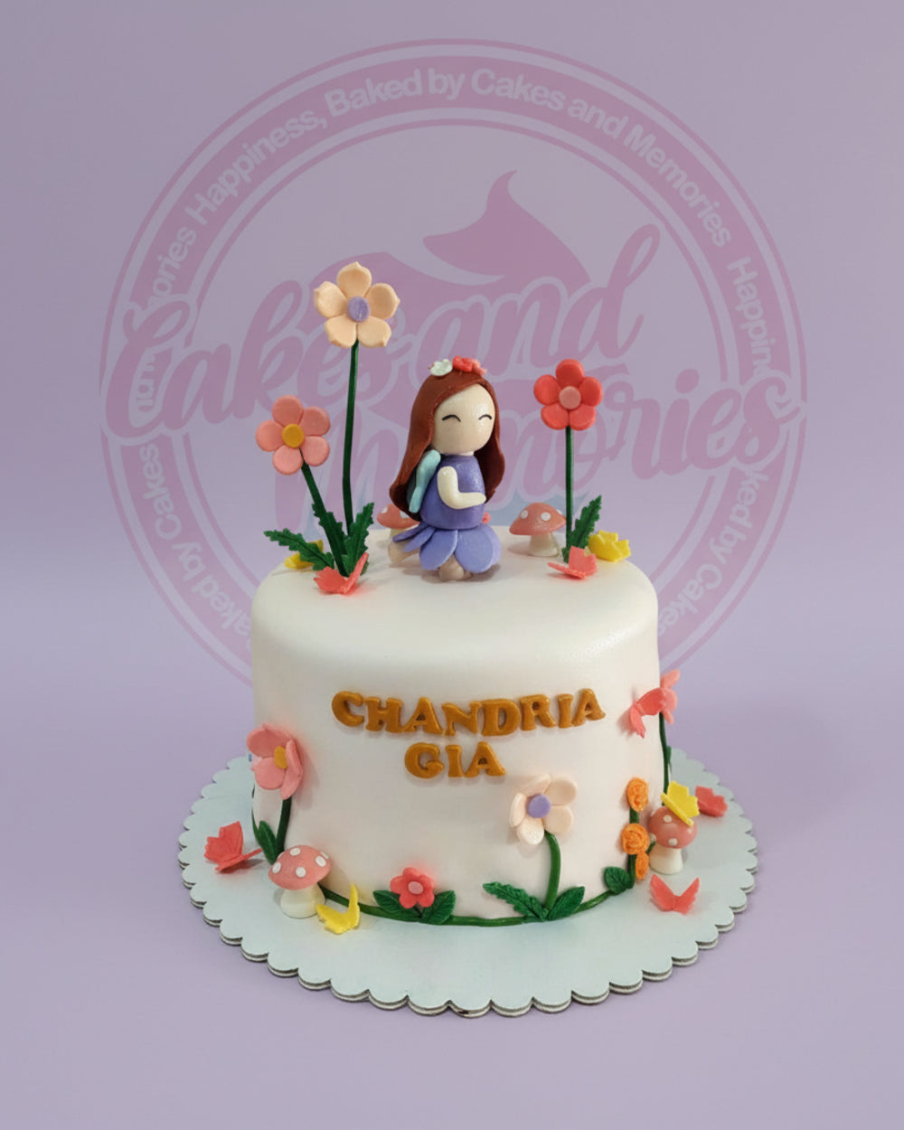 Fondant fairy garden birthday cake with girl fairy, colorful flowers, mushrooms, butterflies, and 'CHANDRIA GIA' on white.