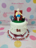 White fondant 84th birthday cake for Nanay Ester, featuring an elderly woman topper in a red armchair with a walker.