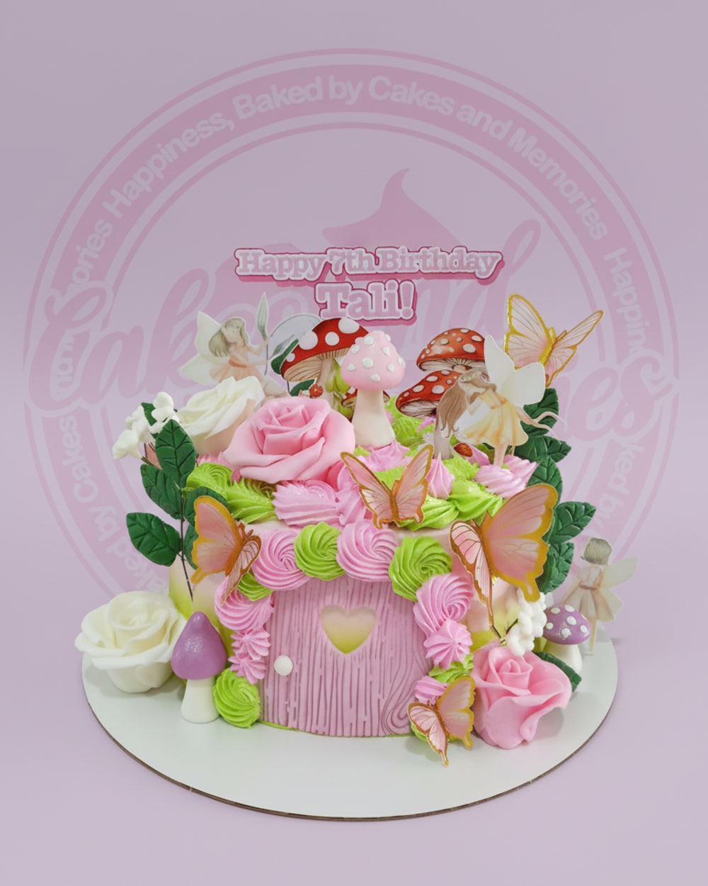 One-tier fairy birthday cake with a pink fairy house, buttercream swirls, mushrooms, fairies, butterflies, and roses. Text: Happy 7th Birthday Tali!
