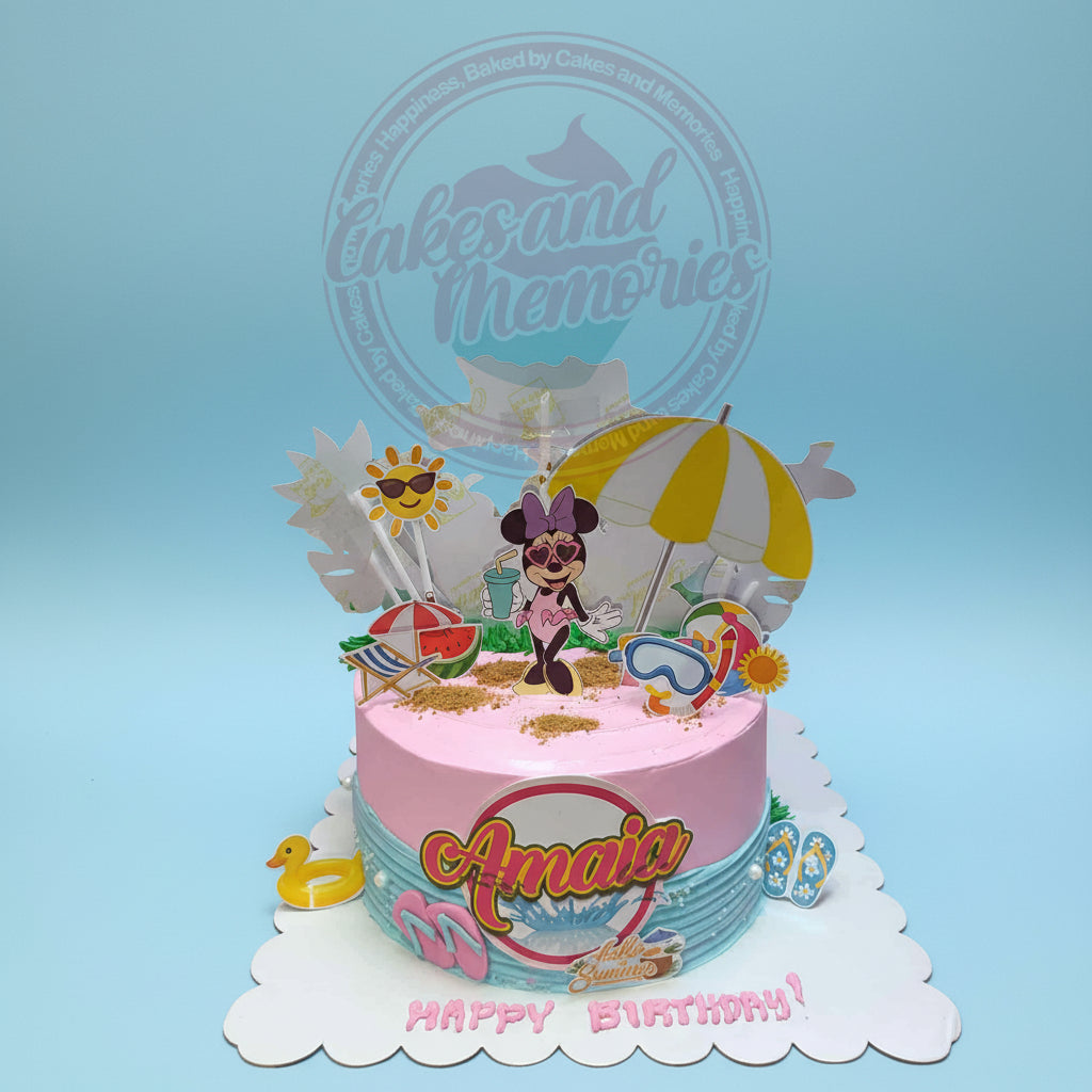 One-tier Minnie Mouse birthday cake with beach theme toppers, 'Amaia' plaque, pink & blue icing, and 'Happy Birthday!' text.