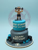 Two-tier fondant birthday cake with a fitness theme, featuring a man lifting weights, gym equipment, and messages in blue, gray, and white.