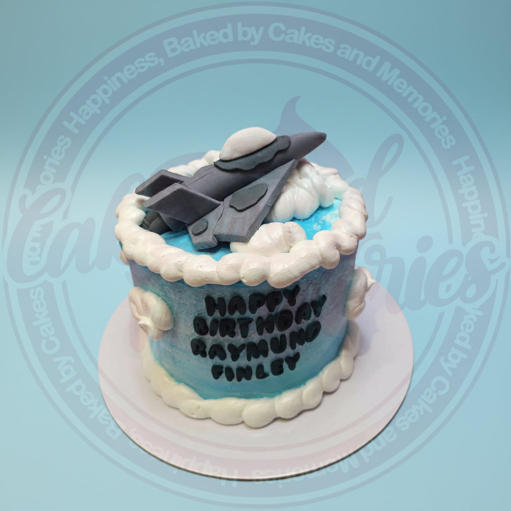 One-tier custom airplane birthday cake with a grey fighter jet topper, white clouds, and 'Happy Birthday Raymund Finley' text.