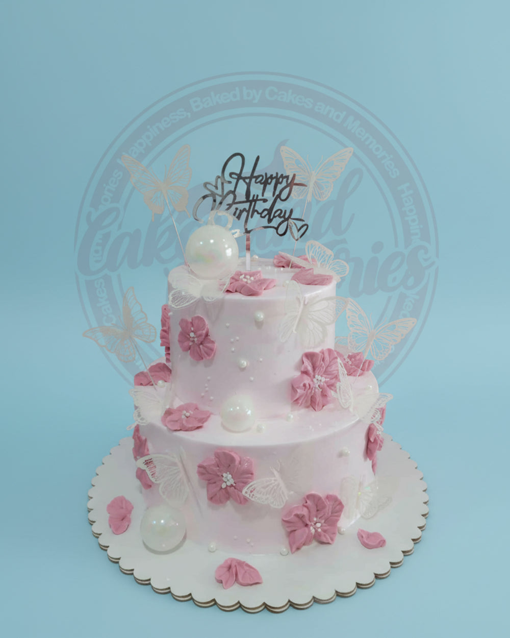 Two-tier pink birthday cake adorned with delicate white butterflies, pink fondant flowers, and shimmering pearls, topped with 'Happy Birthday'.