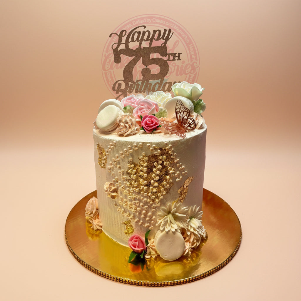 Elegant 1-tier buttercream birthday cake with gold leaf, piped details, pastel flowers, macarons, and a 'Happy 75th Birthday' topper.