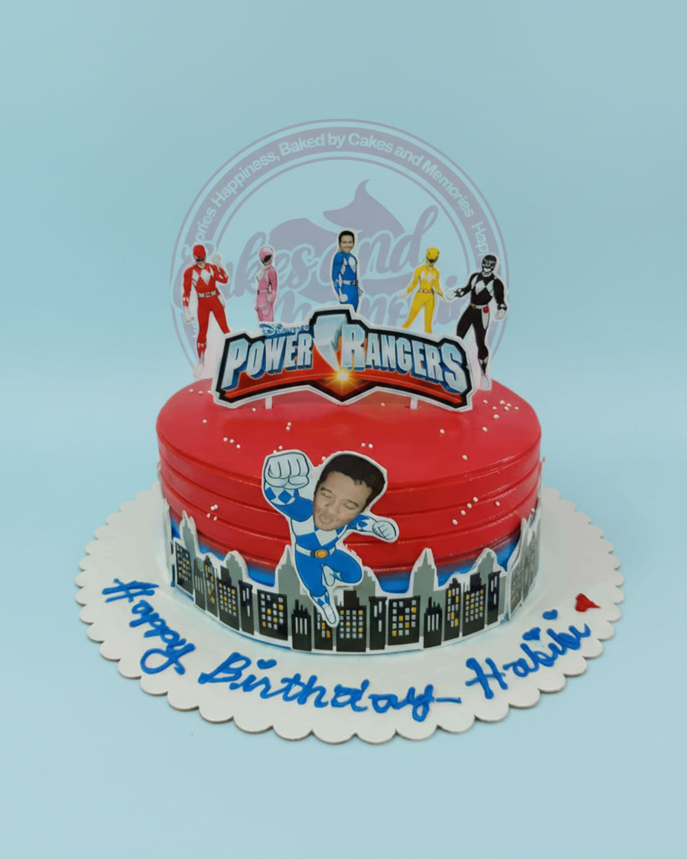 One-tier red Power Rangers birthday cake with city skyline wrap, Power Rangers toppers, and "Happy Birthday Habibi" text.