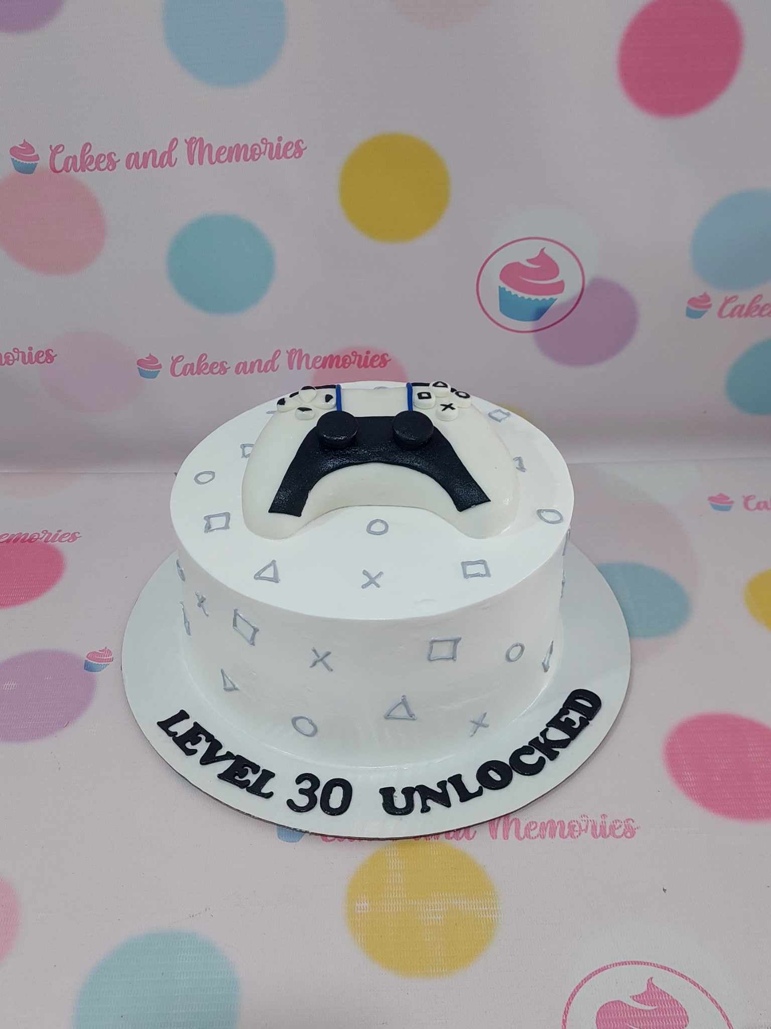 One-tier gaming cake with black & white PlayStation controller, grey symbols, and "Level 30 Unlocked" text.