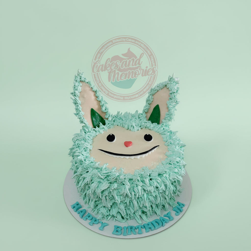 One-tier custom birthday cake featuring a cute mint green fuzzy monster with a friendly smile, personalized with 'HAPPY BIRTHDAY JIA'.