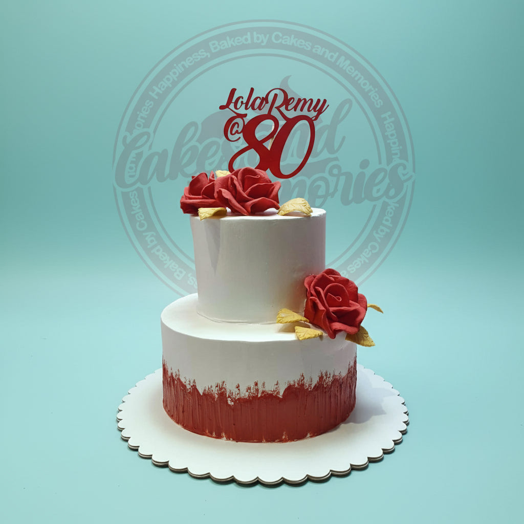 Two-tier custom birthday cake for Lola Remy's 80th with red roses, golden leaves, and a red topper, in white and red.
