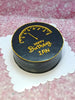 Round birthday cake with speedometer design, 'Happy Birthday Ian' text, black icing, gold piping on white board.