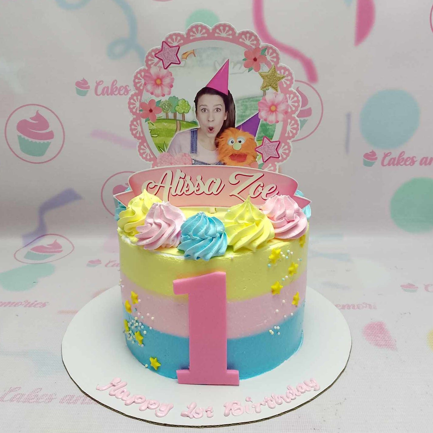 Introducing the charming Ms. Rachel Cake, featuring a delightful pastel yellow, pink, and blue palette perfect for any baby or toddler nursery theme. This beautifully decorated 1-tier cake is ideal for celebrating special moments inspired by Miss Rachel's engaging YouTube videos.