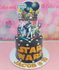 This custom Star Wars cake features a striking black and gold design, adorned with themed printout toppers of characters like Darth Vader, Yoda, and Chewbacca, perfect for a 10th birthday celebration. The cake is topped with lightsaber accents and a decorative Death Star, capturing the essence of the galaxy far, far away for any young Jedi fan.