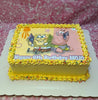 This custom Spongebob Cake celebrates Mojo's 6th birthday with a colorful design featuring an edible photographic print of SpongeBob Squarepants and Patrick Star, adorned with shells, starfish, and sprinkles in shades of yellow and pink. The rectangular cake is a perfect centerpiece for any themed celebration.