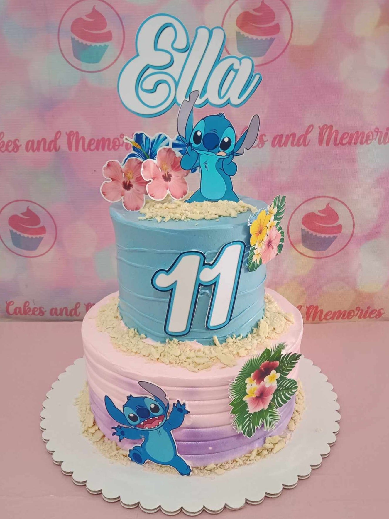 This stunning two-tiered Lilo and Stitch cake features shades of blue, pink, and purple, adorned with playful sprinkles and a cheerful number eleven, perfect for an 11th birthday celebration. The design incorporates tropical floral elements and ocean themes, capturing the essence of a summer beach party with Disney charm.