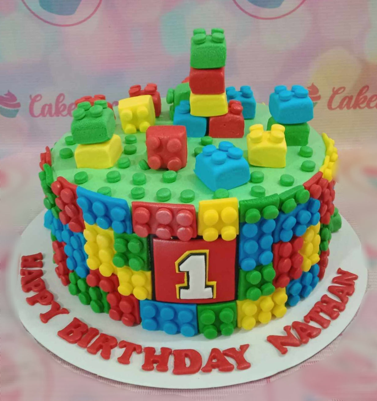 A colorful Lego-themed cake featuring green, red, yellow, and blue blocks, perfect for a child's 1st birthday celebration. This 1-tier cake is adorned with fun printout toppers, bringing the joy of toys to the dessert table.