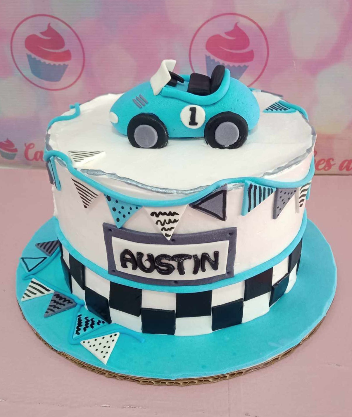 This stunning Wheels Cake features a vibrant blue and teal design with white accents, perfect for a toddler's 1st birthday celebration. Snazzy racing elements pay homage to classic cars like Ferrari and Lamborghini, making it a delightful centerpiece for any young car enthusiast's party.