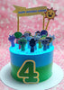 This eye-catching birthday cake features a blue and green ombre design adorned with sprunky cartoon characters and a sun, perfect for a 4th birthday celebration. Topped with a yellow banner and printout toppers from popular horror video games, it's a fun centerpiece for the birthday boy's special day.