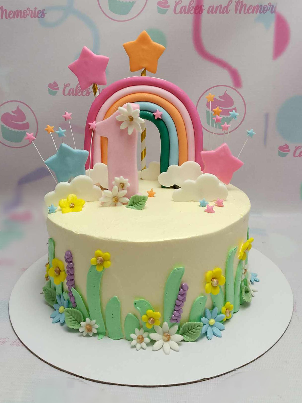 A stunning rainbow cake featuring an edible rainbow topper, delicate stars, and a playful number one, perfect for a toddler's 1st birthday celebration. Surrounded by a garden of floral designs and soft clouds, this one-tier cake is a colorful centerpiece for any birthday gathering.