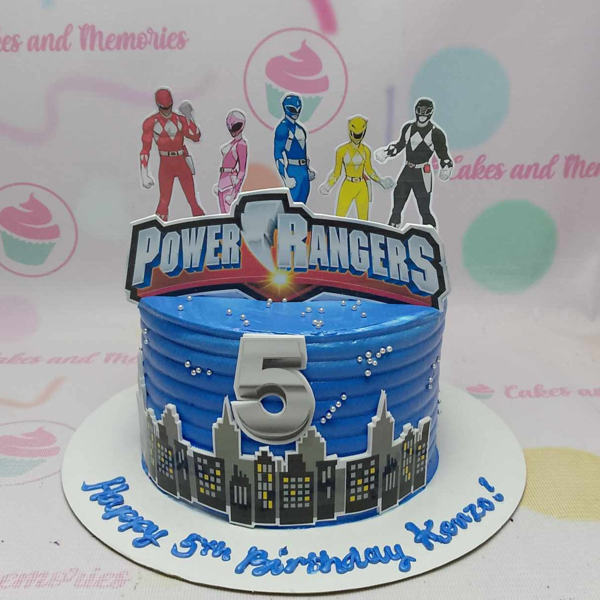 Celebrate your little one's 5th birthday with a vibrant Power Rangers Cake, featuring a royal blue design and an exciting city skyline. Adorned with printout toppers of beloved super heroes Zordon and Alfalfa, this 1-tier cake brings the thrilling world of the Power Rangers to life!