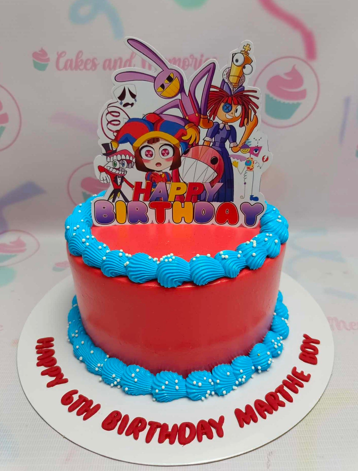 A colorful Digital Circus Cake featuring red and blue hues, decorated with cartoon digital circus characters, and topped with white sprinkles. Perfect for a 6th birthday celebration, it showcases printout toppers on a single tier design.