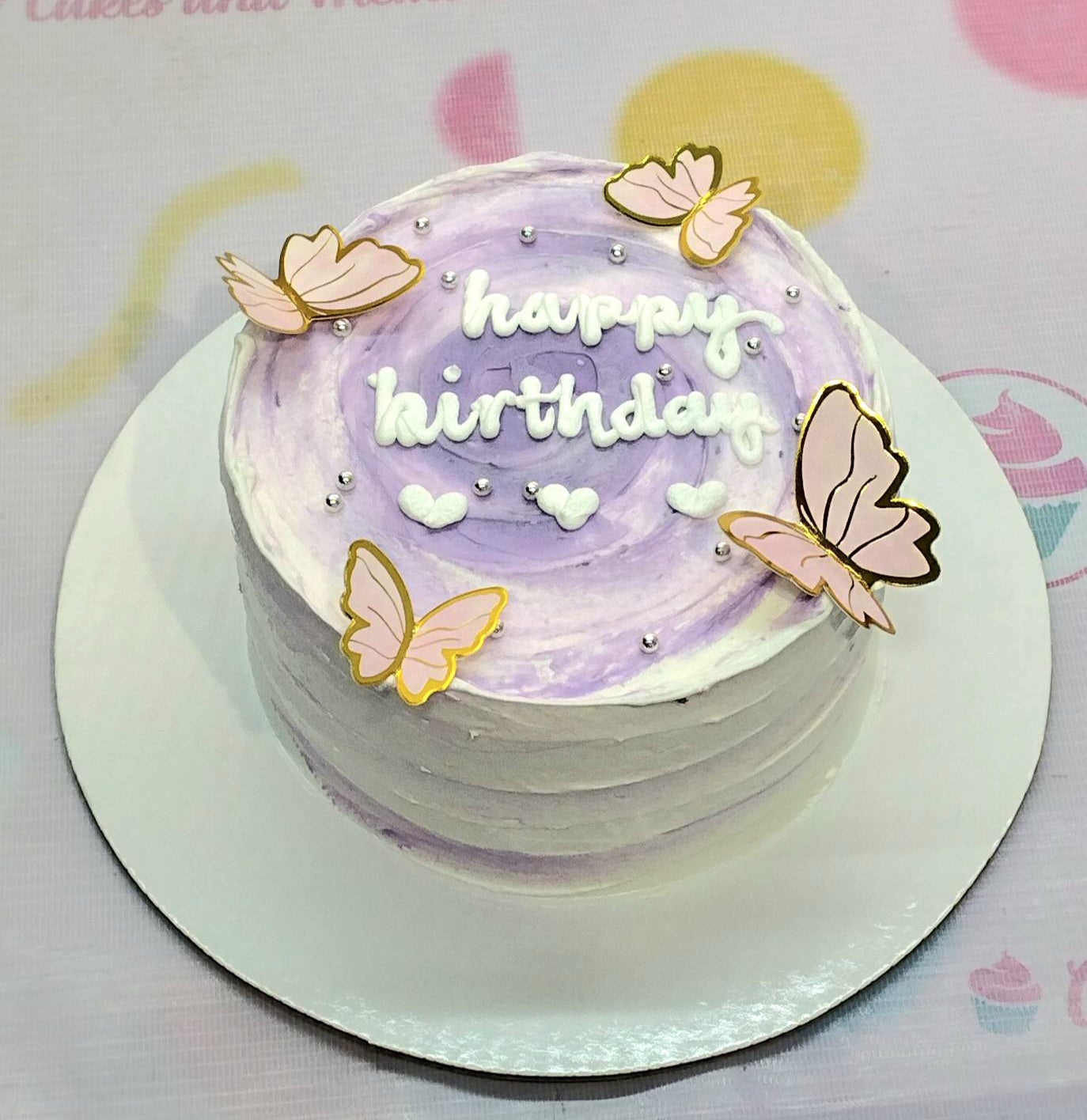 This enchanting Butterflies Cake features a rich purple swirl design, adorned with pink butterfly accents, heart motifs, and silver sprinkles. Perfect for a girl's birthday celebration, this one-tier cake is topped with cute printout toppers for an added touch.