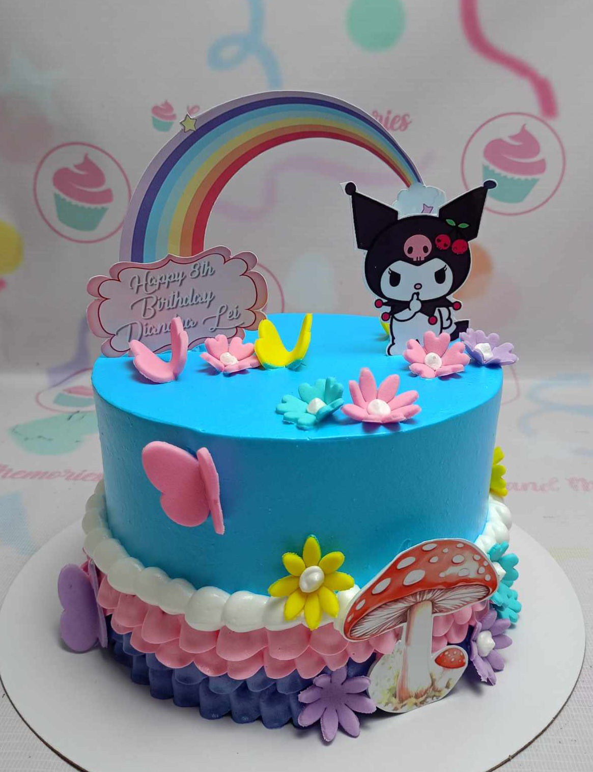 This charming Kuromi Cake features a stunning blend of blue, pink, and purple with delightful yellow flowers, a printout rainbow, butterflies, and mushrooms, perfect for an 8th birthday girl. The single-tier design is adorned with decorative printout toppers, making it a lovely centerpiece for any celebration.