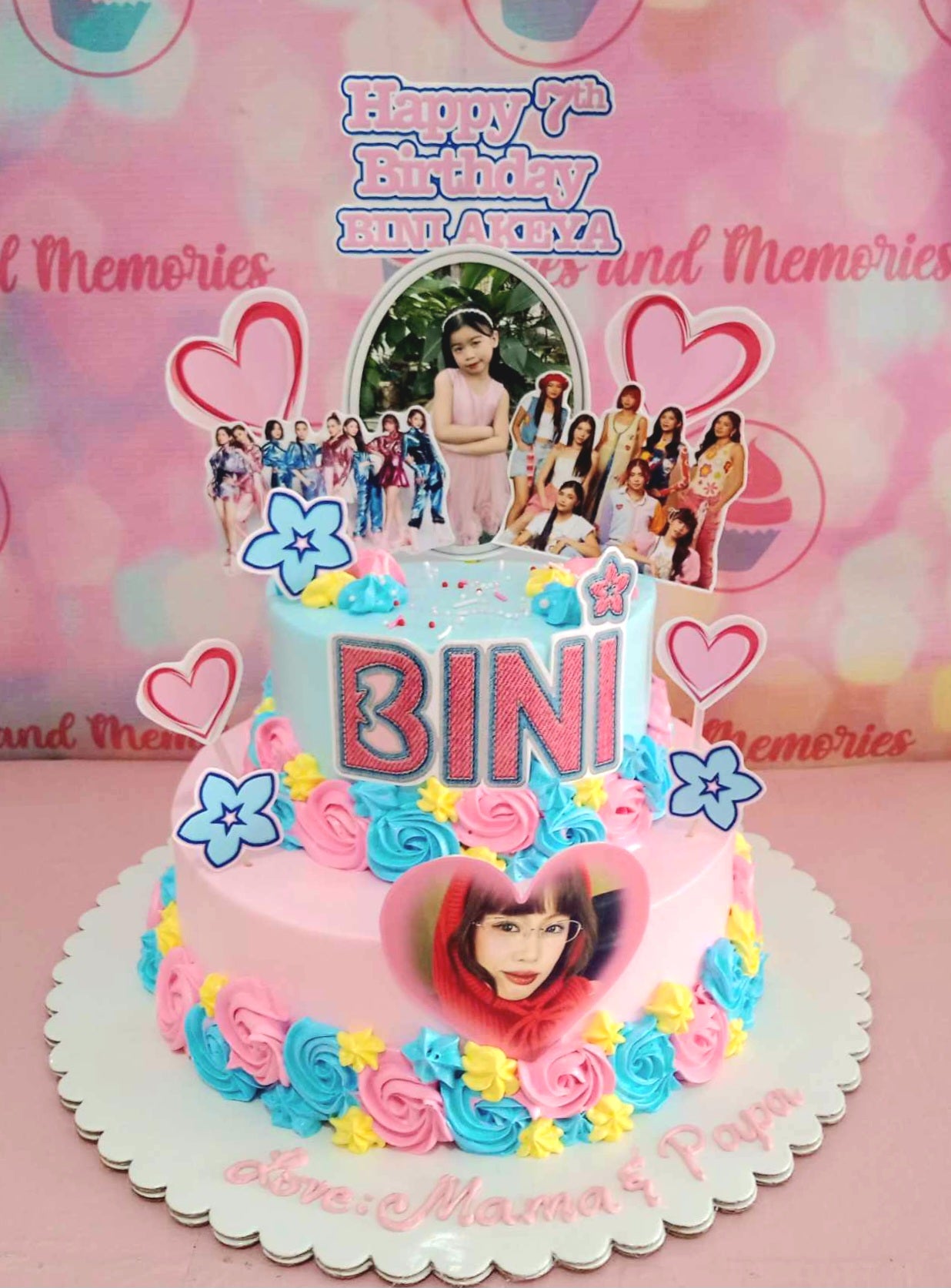 The Bini Cake features two tiers adorned with pastel blue and pink hues, intricately decorated with charming pink hearts and delicate blue blooms. Perfect for fans of K-pop and P-pop, this custom cake captures the spirit of Bini's music and style.